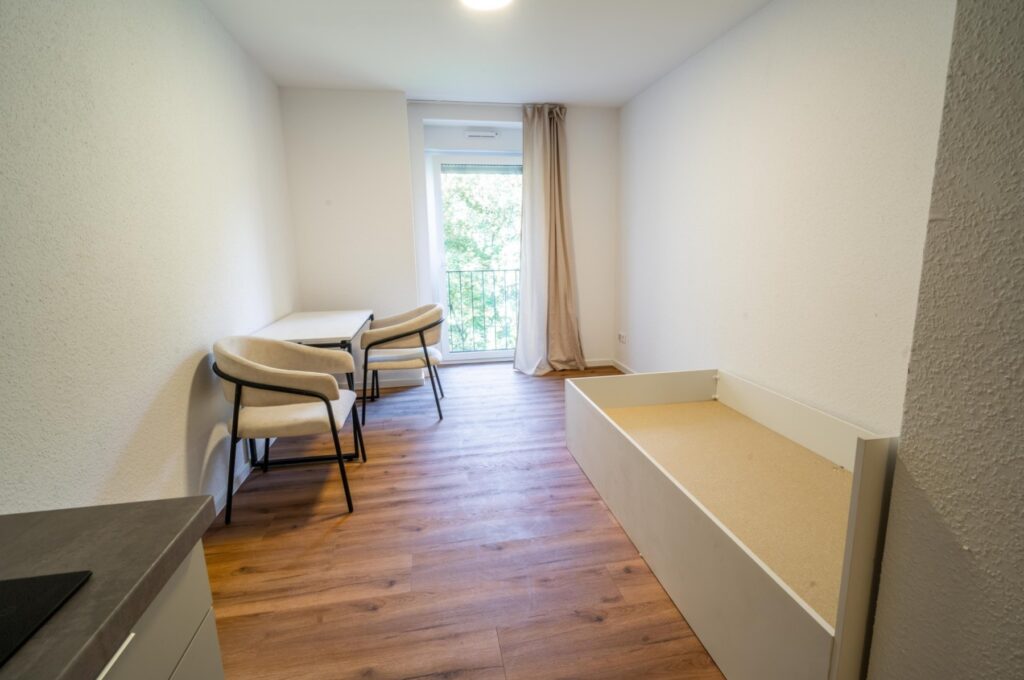 Wohnraum mit Fenster, Tisch und Bettgestell bei Ankunft (echtes Foto)